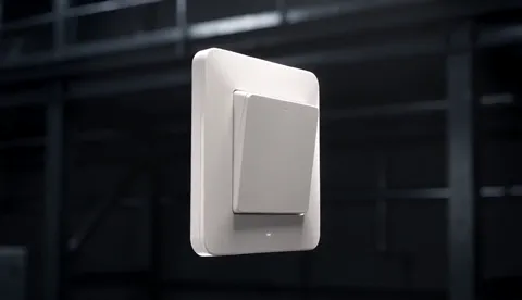 A light switch hangs in the air against a dark industrial ground: a white plate, a large rocker, soft radii. Light from 