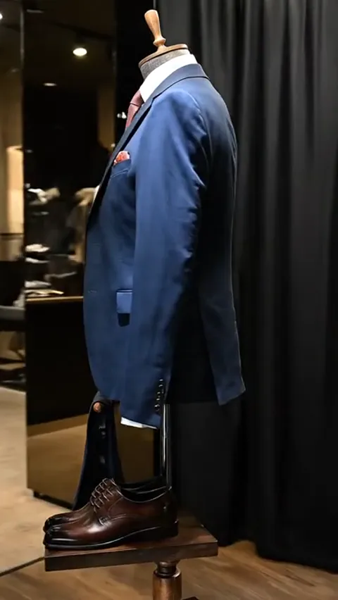 The mannequin turns, the suit in profile. The waistcoat is close-fitting while the jacket sits looser — the difference b