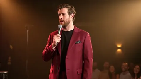 Closer: the jacket is loose, the shoulder dropped, the lapel wide. The suit deliberately does not follow the body — that