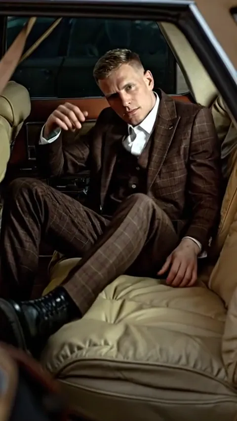 He raises himself, framed to the hip. The waistcoat under the jacket is visible, and the check behaves at the fold — the