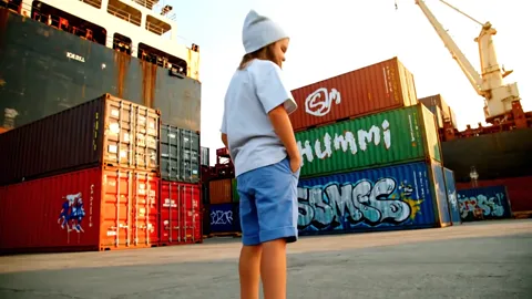 She turns her back, framed at three-quarters. The length of the t-shirt against the shorts is visible, and the back carr
